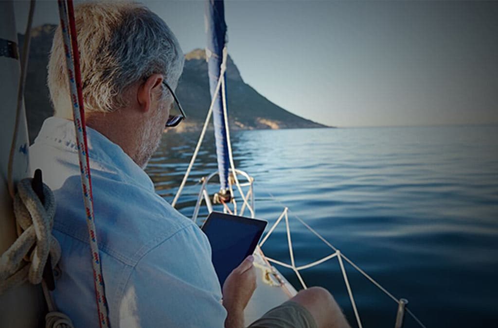 Older man relaxing on a sailboat while looking at a tablet
