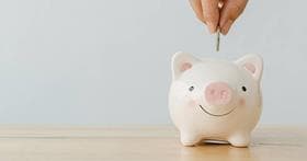 A hand putting coins in a piggy bank