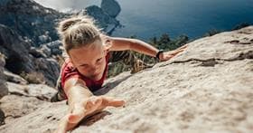 Young woman climber climbing up a stone wall overcoming obstacles